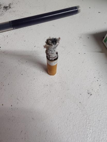 Photo of a finished cigarette placed orthogonally on the table to silently burn out caus no Ashtray available...
