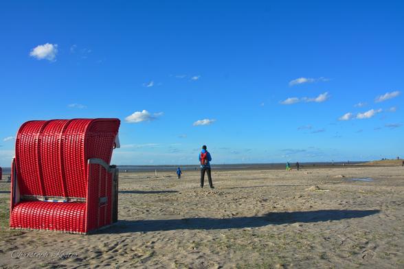In the foreground on the left is a bright red beach chair. Some distance away is a person looking out to sea from the beach. Scattered clouds can be seen in the sky (original coloured version).
