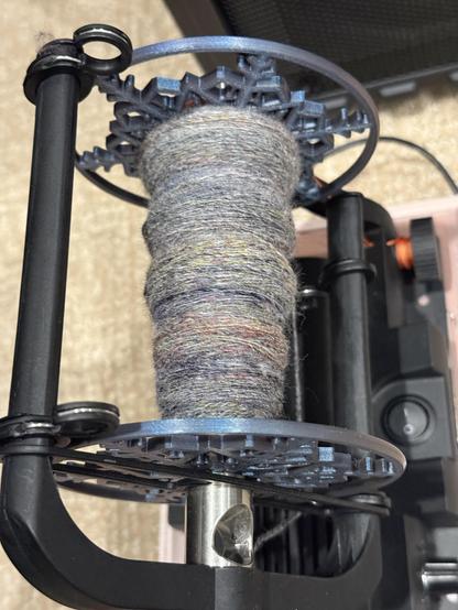 Partially filled bobbin on an e-spinner with a 2 ply yarn. Cooler ranges from grey to white with pops of yellow and red.