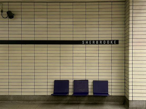 On a tiled wall, the name of a Montreal subway station appears above a row of three benches.