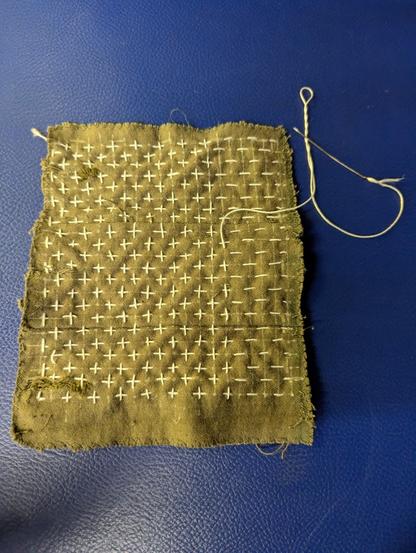A piece of fabric with sashiko-style embroidery on it. Crosses have been made by overlapping thread with existing lines.