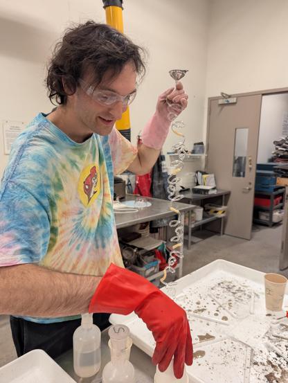 me, wearing red and pink kitchen gloves, with a funnel, and all the fire polished lols attached end to end with latex tubing hanging down. bottles of chemicals and  messy dryer pan are on the table.