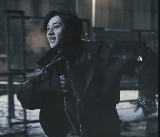 Bang Chan running through a snowy industrial environment at night. He's wearing a dogtag pendant on a chain.