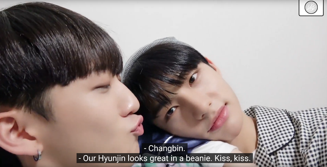 Hyunjin rests his head on Changbin's shoulder. Changbin turns his head towards Hyunjin and purses his lips for a kiss. Caption: "Changbin." "Our Hyunjin looks great in a beanie. Kiss, kiss."