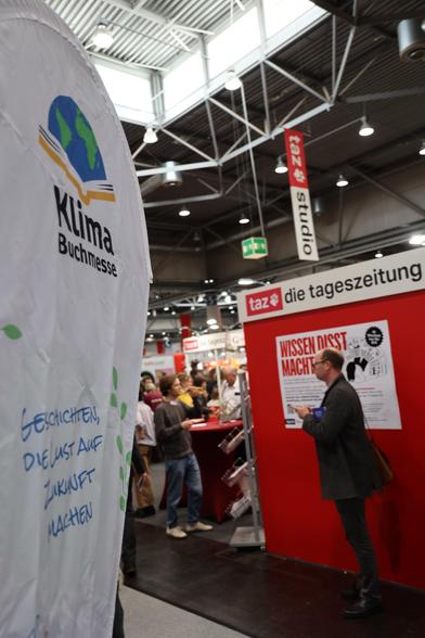 Im Vordergrund die Beachflag der Klimabuchmesse, im Hintergrund der Messestand der Taz die Tageszeitung