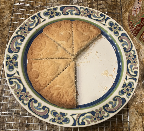 Shortbread with a cute pattern embossed on top (hearts and leaves and curly lines) on a white plate with blue and green floral decoration on rim