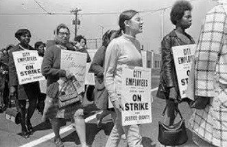 Striking Atlanta sanitation workers, and supporters, walking the picket line, carrying signs that say, “City Workers On Strike.”