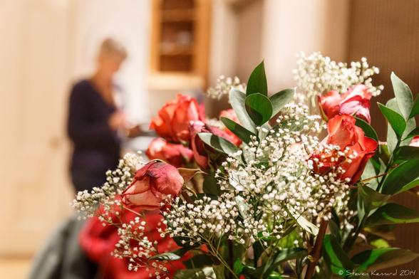 A bouquet of tiny white lowers and bright red ones in a kitchen setting. Behind, out of focus, is a woman in a dark sweater.