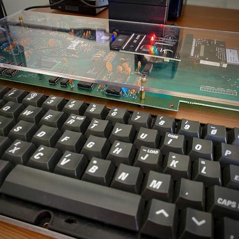 A ZX Spectrum +3e main board in a clear Perspex sandwich (in lieu of its original case). Inside can be seen all the gubbins including a new IDE interface with a bright red LED.