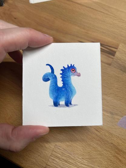 a tiny blue dragon painting with orangey red eyes and a twirly tail