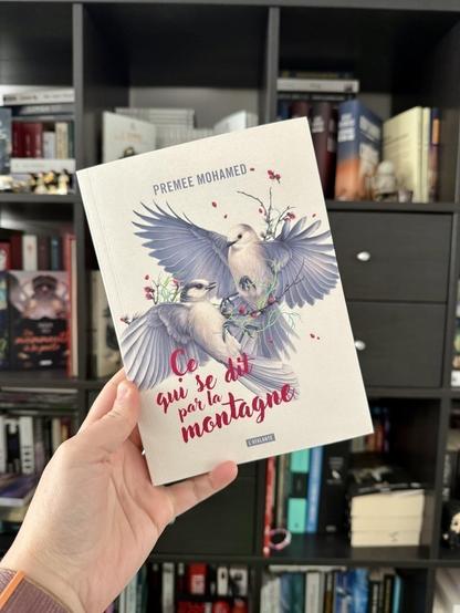 La couverture de Ce qui se dit par la montagne montre deux oiseaux gris bleutés en vol avec des branches à baies rouges.