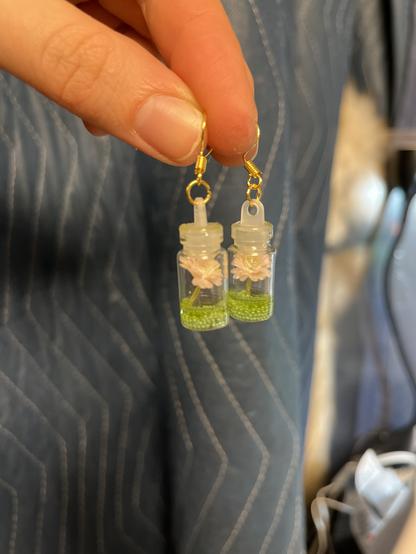 A pair of tiny pink flowers in bottles with resin in the bottom made into earrings