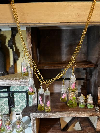 Tiny cherry blossom branch bottle earrings and pendants photographed in front of a dollhouse