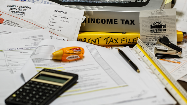 A lot of papers, a few tax books, a receipt, whiteout, a ruler, a pen, a calculator, and a staple remover