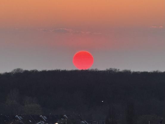 The red sun ball just hovering on the horizon before sunset.