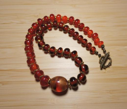 Image of my handmade lampwork hot glass necklace in transparent red and topaz, set against a light wood background.