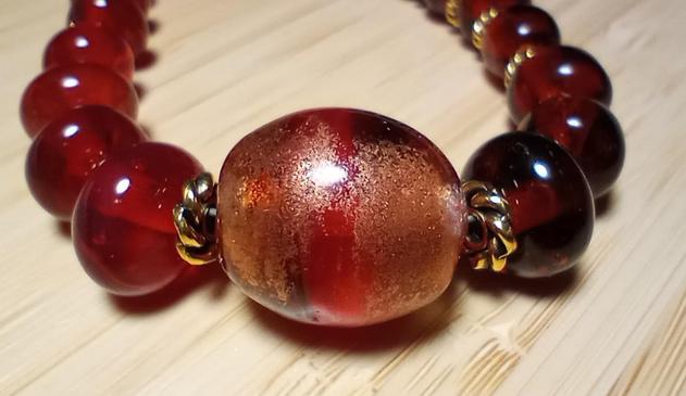 Close up image of the focal bead from my handmade lampwork hot glass necklace in transparent red and topaz, set against a light wood background.