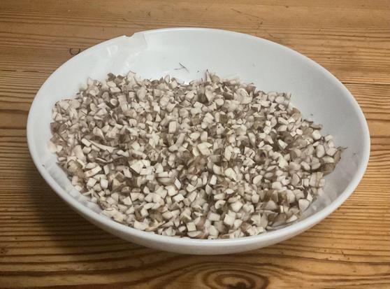 White bowl on wooden table. Bowl contains finely chopped dandelion root
