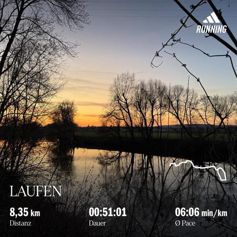 Blick über einen Fluss (Saale), eingerahmt von Sträuchern und Bäumen (ohne Blätter), orangefarbene Abendhimmel, keine Wolken und am Horizont ist eine Siedlung (Schellsitz) mit einer Kirche erkennbar