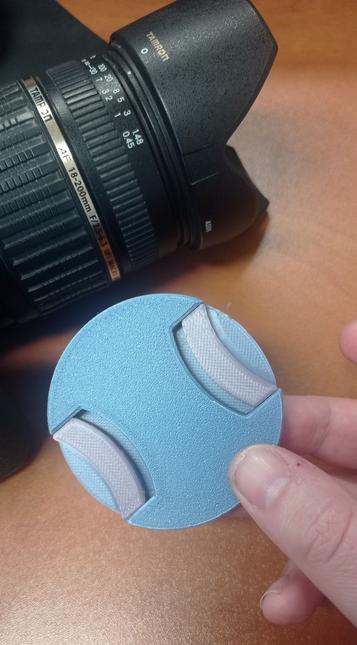 Photo d'un capuchon imprimé en 3d pour d'appareil photo type reflex. Couleur bleu-violet inhabituelle pour ce type d'objet, on voit la texture et les petits défauts typique de ce genre d'impression.