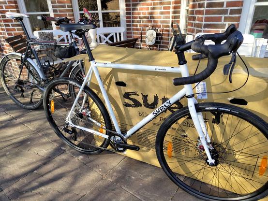 Mein alter grauer Drahtesel im Hintergrund, hinter dem Versandkarton und neuem strahlend weißem Allroad-Bike auf sonniger Terrasse.