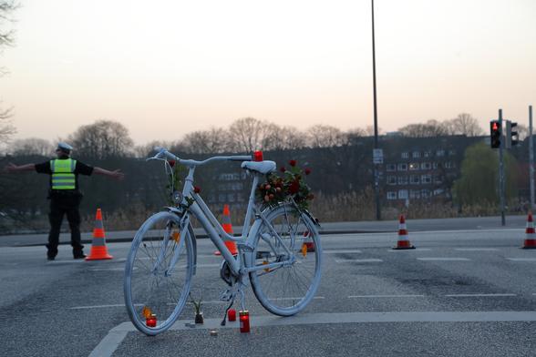 Ein weiß lackiertes Ghostbike steht während der Mahnwache auf der Kreuzung am Jensendedamm in Kiel. Ein Polizist steht im Hintergrund.