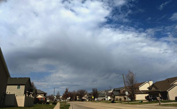 Complex and bubbly white and gray clouds in a blue sky above a street with houses