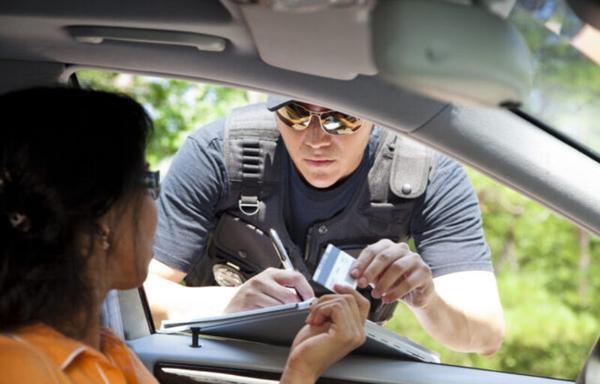 Image of a policeman leaning into the driver’s side window of a car, writing a citation.