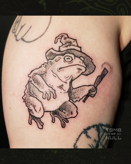 Photo of a fresh tattoo of a frog in a wizard hat with a little stick wand on light skin.