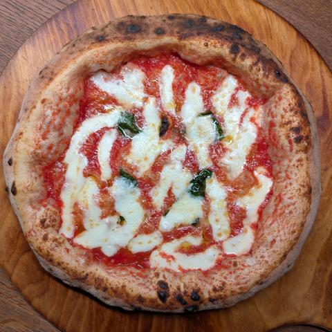 A Pizza Napoletana with an big and airy crust on a wooden plate. It's the queen of Pizza, a Margherita.