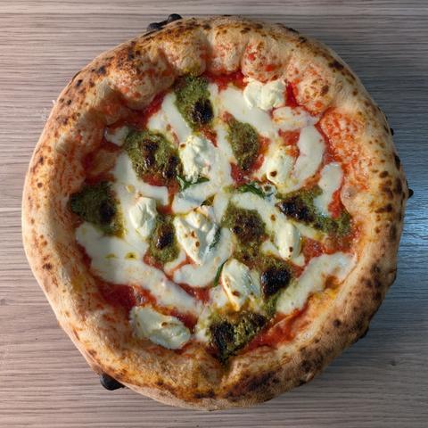 A Pizza Napoletana with an big and airy crust on the kitchen counter. It's topped with pistachio pesto and Mascarpone.