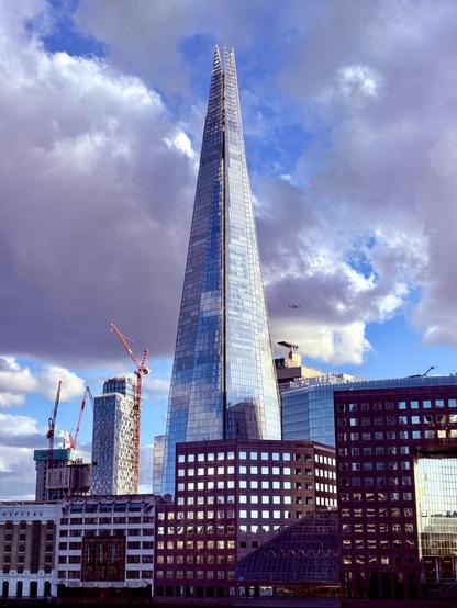 A view of the Shard building in London during the magic hour with smaller buildings on the side beneath a cloudy sky
