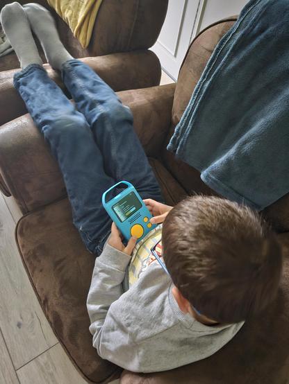 Numéro assis de travers sur son fauteuil toujours sur son lecteur audio et chassant des dinosaures. Plaid sur le côté