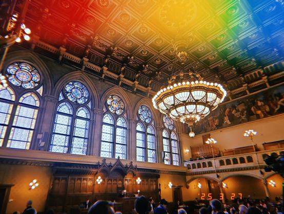 A giant chandelier in a crowded vintage looking hall in gothic revival architecture.