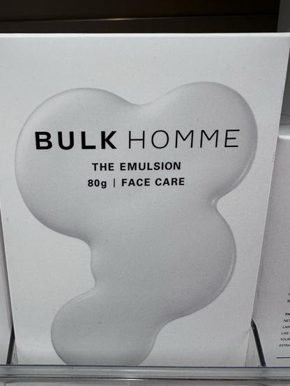 An advertisement for BULK HOMME's "THE EMULSION," an 80g face care product, is displayed on a white background featuring a stylized, watery shape.