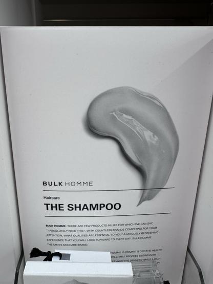 The image features a product display for "The Shampoo" by Bulk Homme. It includes an artistic depiction of a shampoo texture alongside informational text about the brand's commitment to quality hair care for men. The overall design is minimalistic with a focus on the