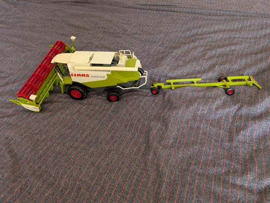 Ein grün/weißer Spielzeugmähdrescher der Firma SIKU mit einem Anhänger, um das Mähwerk zu transportieren.