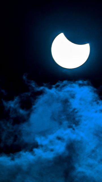 Die Sonne wird vom Mond teilverdeckt. Im Vordergrund sind Wolken.