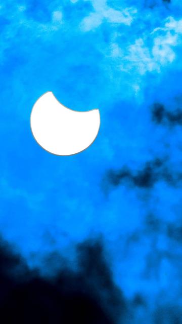 Die Sonne wird vom Mond teilverdeckt. Im Vordergrund sind Wolken.