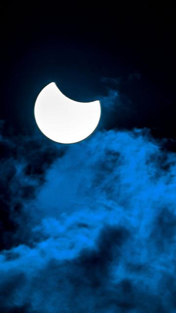 Die Sonne wird vom Mond teilverdeckt. Im Vordergrund sind Wolken.