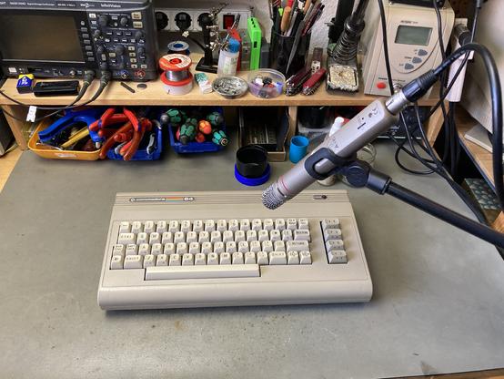 An ALDI Commodore 64 on my workbench with an AKG C1000S microphone on a stand pointing at it. My tools are visible in the background.