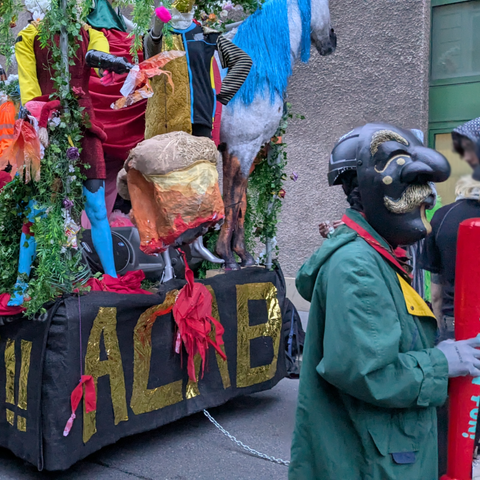 A carnival float has the writing ACAB in gold on the back, in front stands a masked reveller with a black mask typical of the carnival in Basel