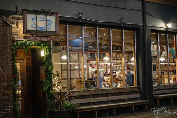 Photograph of the outside of Seattle's Cafe Allegro. In the evening light, customers can be seen inside a cozy looking space enjoying their drinks.
