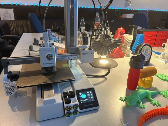 Bambulabs A1 Mini druckt eine Eule. Daneben diverse 3D-gedruckte Modelle