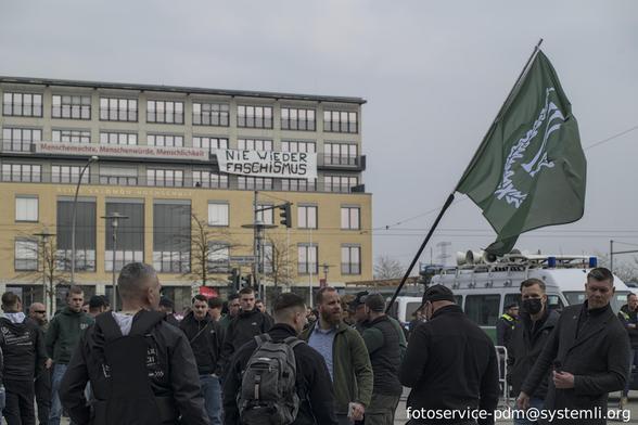 im vordergrund neonazis kundgebung mit der fahne des driteen wegs, im hintergrund die alice-salomon-hochschule an dessen fassade zwei transpaente hängen: "menschenrechte, menschenwürde, menschlichkeit" und "nie wieder faschismus"
