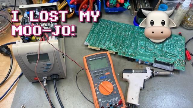 Thumbnail for my video. My desoldering station (with the lid of the case opened), my multimeter (with the leads attached to the desoldering station pump motor) and a random C64 circuit board on my workbench. The overlayed text reads "I LOST MY MOO-JO!" and a cow emoji is pictured next to the text.