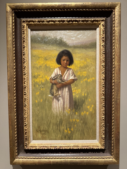 photo of the painting in gold frame on display at museum Portrait in long vertical format of a young Pomo child in pink and white striped clothing holding a jackrabbit while standing in a field of blooming yellow flowers