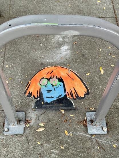 Another Ongo stencil. This one is under a bike rack and just shows Ongo's head. The character has wild hair and a new age art style, similar to Andy Warhol's look, but with Danny DeVito's face.