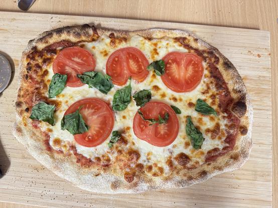 Eine Pizza mit Käse, Tomatenscheiben und Basilikum