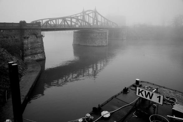 An old, steel harbor bridge that is barely visible in the fog.